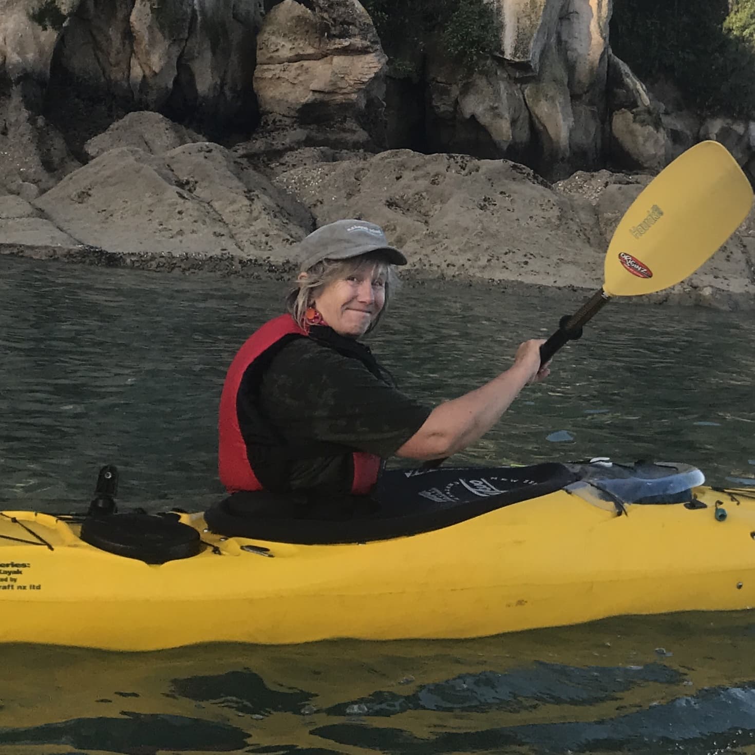woman in kayak on water with rocks behind